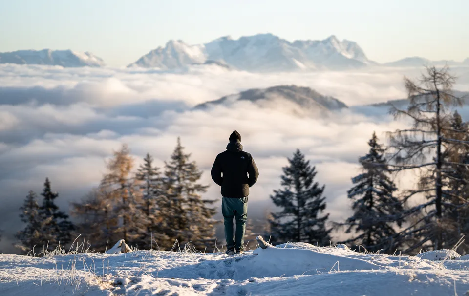 Person steht allein auf einem verschneiten Gipfel über einem Wolkenmeer