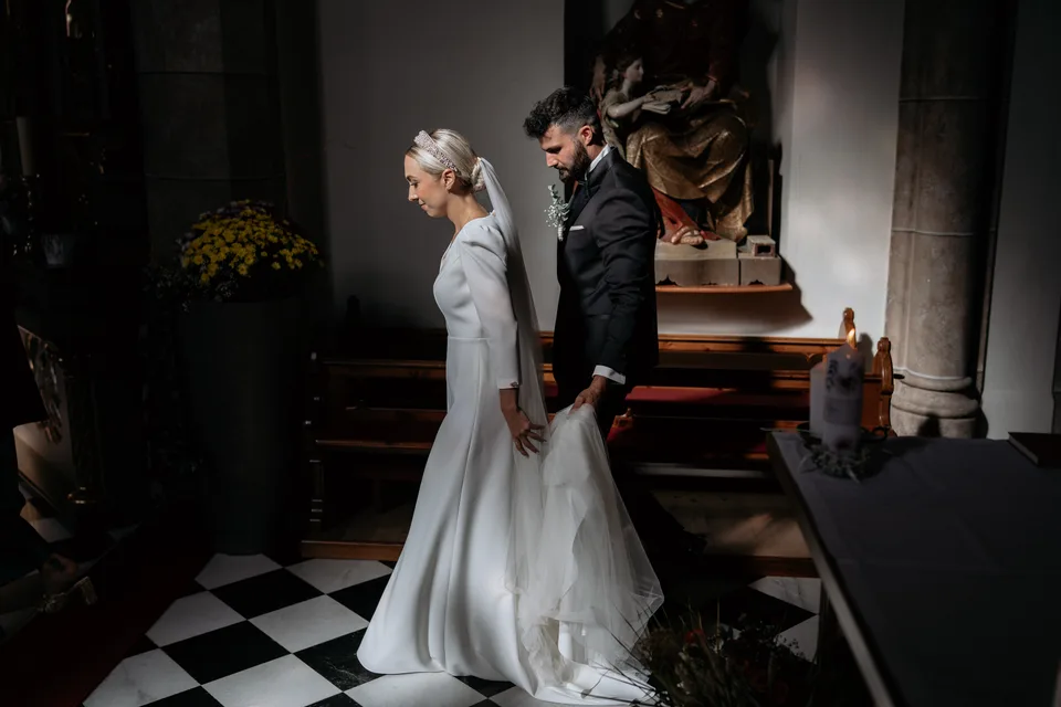 Brautpaar steht bei der Trauung vor dem Altar auf einem Boden aus schwarzweißen Fliesen